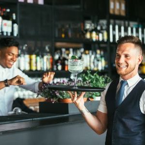 Immagine che mostra una ragazzo mentre porta un cocktail su un vassoio. È usata come immagine del corso gratuito "ADDETTO SALA E CAMERIERE" del progetto GOL