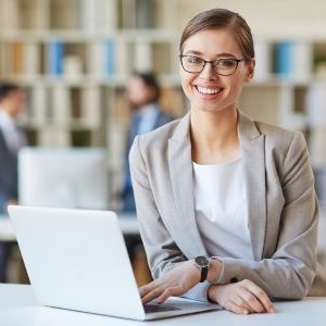 Immagine che mostra una ragazza sorridente sui 35 anni mentre è al computer. È usata come immagine del corso gratuito "SEGRETARIO/A" del progetto GOL